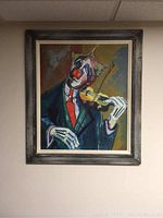 Framed painting of clown playing violin hung on a wall.