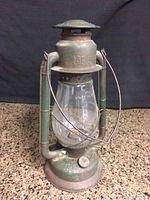 Full view of the vintage green Beacon GSW barn lantern sitting on a rough surface, showing the clear glass globe and metal handle.