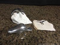 Three Hoselton sculptures on countertop. Large polished metal beaver and two metal birds on white stone bases.