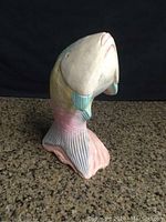 Side view of a solid wood fish sculpture on a granite surface against a black background, showing painted pastel colors and wooden texture.