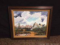 Full view of the framed painting showcasing the landscape scene with mountains, clouds, cacti, and desert shrubbery.