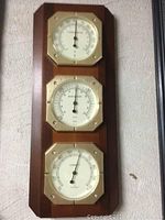Full view of the wooden plaque holding all three instruments mounted on the wall showing thermometer (top), barometer (middle), and humidity meter (bottom).