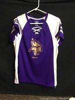 Front view of purple and white Minnesota Vikings women's jersey with laced neckline and team logo.