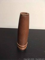 Side view of brown metal artillery shell with copper colored base on black surface