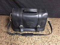 Front view of the black leather Bugatti carrying bag showing dual buckle straps and top handle.