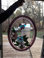 Oval stained glass panel held up in front of window showing butterfly and flowers design.