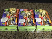 Three full unopened boxes of Johnny Quest playing card packs with each box containing 48 packs visible on countertop.