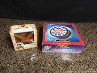 Photo of two game boxes on granite counter: DaVinci wooden helicopter puzzle in vintage map box, Hockey Night in Canada boxed car game.