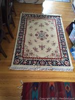 Full view of rectangular carpet on hardwood floor showing floral center design and fringe along the shorter side.
