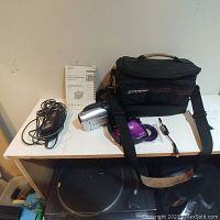 Sony Handycam, black carrying case, power adapter, remote control, video cable, and Operating Guide on a table against a wall.
