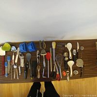 Top view of a row of various kitchen utensils and gadgets laid out on a table showing spatulas, peelers, tongs, whisks, and more.