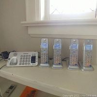 Overall view of Panasonic base unit and four handsets on charging bases, all powered and showing date/time on screens.