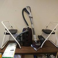 Full lot showing Kenmore canister vacuum cleaner with hose, wand and powerhead plus two white folding step stools and vacuum bags on a wooden table.