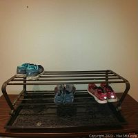 Photo of one metal shoe rack with antique brass finish holding three pairs of shoes on two tiers, with molded drip tray on bottom tier