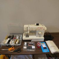 Sewing machine on table with organizer box, spool containers, thread packs, manual and scissors laid out