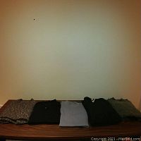 Five men's wool sweaters laid flat on a wooden surface, showing different colors and styles.