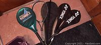 Photo of five racquets arranged on floor, including two Yonex badminton racquets with covers and three tennis racquets, one branded Pro Kennex.