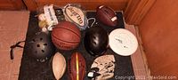 Photo showing a variety of sports equipment including two helmets, several balls, a baseball glove, and a frisbee arranged on floor