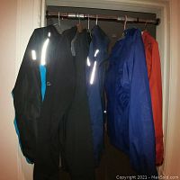Full view of five men's medium jackets hanging on a rod, showing variety of colors and styles including waterproof and softshell jackets.
