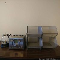 Full view showing Capresso electric kettle, Cuisinart 4-slice toaster, and four wire mesh baskets on a wooden surface against a neutral wall.
