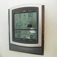 Front view of electronic weather station LCD screen showing temperature, humidity, pressure, weather icons, time, and date