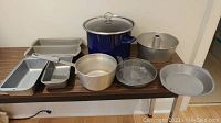 Full view of all cooking supplies including loaf pans, aluminum bowl, tube cake pan, round springform pan, shallow pan, and large blue porcelain pot with lid.