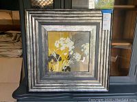 Full view of the square framed hydrangea wall art with a layered silver frame sitting on a black surface.