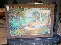 Full view of framed wall art showing hammock on tropical beach scene with palm trees and porch structure.