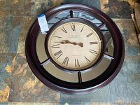 Front view of the round mirrored Roman wall clock showing wooden frame, mirrored panels, and clock face with Roman numerals.