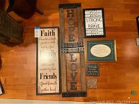 Overview photo showing all six farmhouse metal and wood word art pieces laid out on floor, including large 'HOPE LOVE' piece, rectangular 'Faith Family Friends' plaque, and four smaller plaques