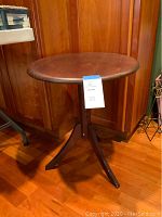 Front view of wood pedestal table showing round top and three-legged base.