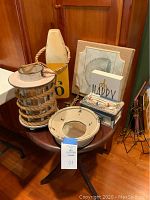 Photo showing the wooden buoy, shell wall art, decorative plate, candle lantern and small decorative sign on a round wooden table against wood paneling.