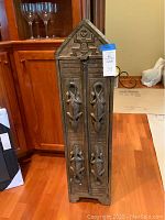 Front view of the tall narrow wooden cabinet with carved gecko decorations on the double doors and pointed top.