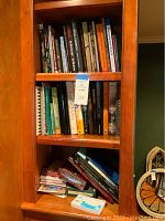 Wooden bookshelf displaying an assortment of novels and cookbooks with various titles and sizes.