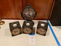Photo showing the scroll style clock and three votive candle holders together on a white surface.