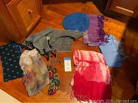 Six scarves arranged on wooden surface showing variety of patterns and colors including a labeled cashmere scarf made in Scotland.
