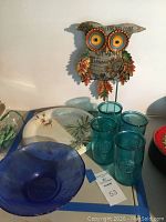 Photo showing melamine plates, blue glass bowl, aqua glasses, and owl table art on surface