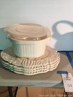 Stack of five turkey-themed cream ceramic plates with autumn motifs, underneath two white microwaveable storage containers with lids on a table.