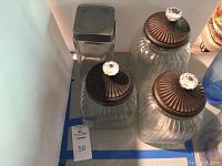 Four glass canisters including three with bronze fluted lids topped with glass knobs and one with a plain metal lid.