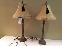 Pair of matching wood table lamps shown with beige fabric bell lampshades and twisted carved wood bases on a white surface.