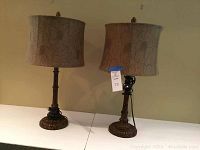 Two bamboo style metal table lamps with beige floral fabric shades on a white table against a neutral wall.