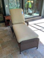 Front angle view of resin wicker reclining lounge chair with beige cushions on tiled floor.