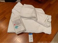 White queen-sized quilt, two pillow shams, and one set of 2 pillow shams in package all displayed on wooden floor