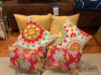 Six outdoor pillows including yellow solid and floral printed cushions arranged on floor in front of couch.