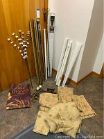 Photo of assorted metal curtain and shower curtain rods leaning against wall with drapery panels and various accessories around base.