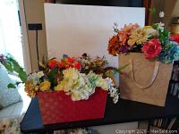 Two containers on a black surface filled with a variety of colorful faux flower stems, including roses, peonies, tulips, hydrangeas, and decorative greenery.