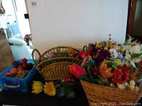 Overview of multiple baskets and blue plastic bin with assorted faux flowers and faux fruit on a table