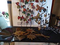 Set of metal art pieces displayed, showing colorful leaf and butterfly wall decor alongside flower-themed metal tray.