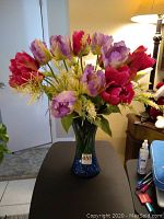 Full view of blue glass vase holding the mixed faux floral silk arrangement with red and purple tulip-shaped flowers and white filler foliage.