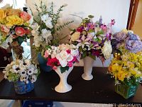 Wide view showing 7 vases or planters each with assorted silk floral arrangements. The flowers include several colors and types, and vases vary in design and color.